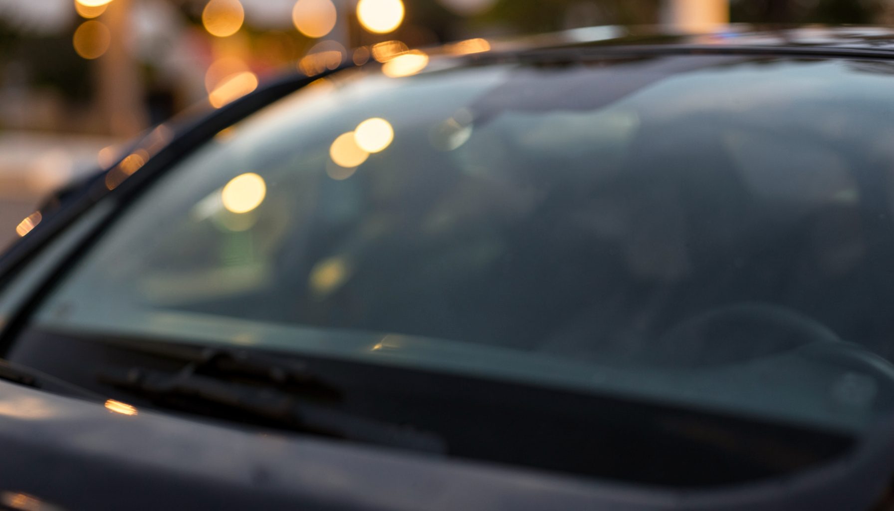 Glossy dark car windshield with soft reflections and warm bokeh lights in the background