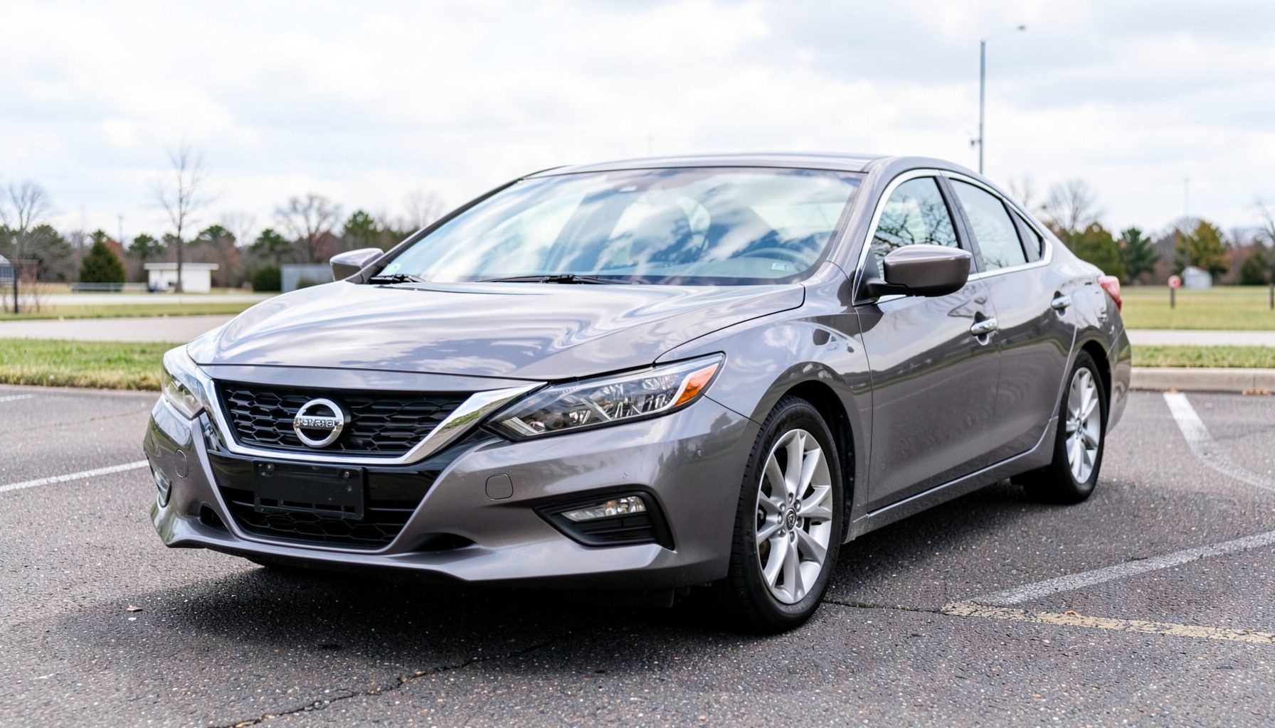 A Nissan Altima midsize sedan on a paved lot, its windshield reflecting a bright overcast sky