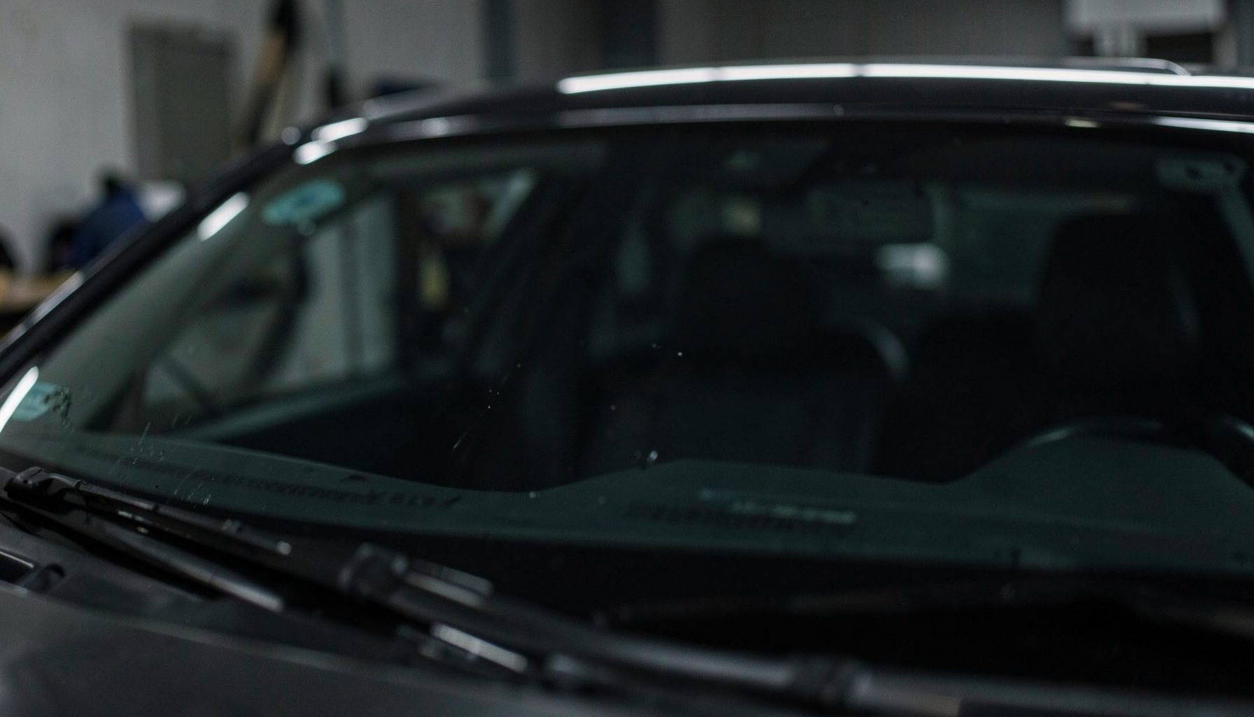 A close-up of a car windshield being professionally repaired, with soft workshop lighting and a dark, focused atmosphere