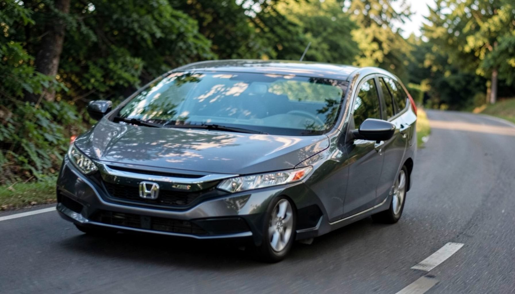 A Honda Civic compact car on a quiet road, its sloped windshield visible with gentle reflections of trees and sky